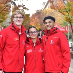 A group of diverse student leaders at St. John’s University, smiling and engaged in conversation outdoors on campus, representing various leadership roles such as student government, peer mentors, and student ambassadors.